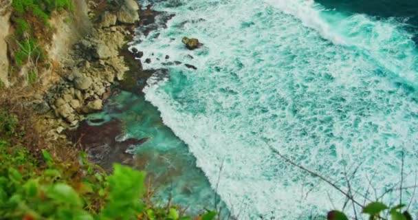 岩の多い海岸の広い波の中で浅い鮮やかな緑の玉青い海の水のロール 手前の緑がクローズアップされた静的な上からの眺め ウルワツ バリ島 パラダイスビーチ — ストック動画