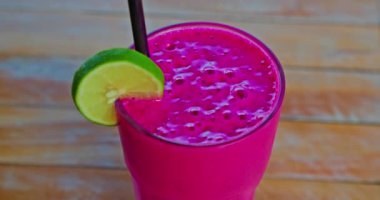 Pitaya ejderhası meyve suyu. Ahşap masa arkasında taze meyve suyu. Limon dilimi ve siyah plastik kamış. Yakın çekim, el kamerası görüntüleri. Şeffaf cam..