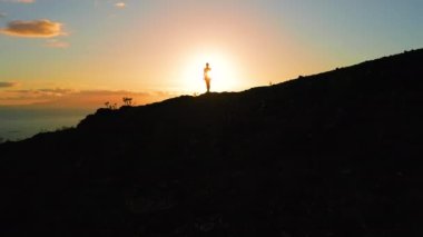 Güneş ışınlarıyla aydınlatılan kız silueti deniz manzarası günbatımı arka planında karanlık doğal dağ kayalıklarıyla aydınlanıyor. Gökyüzü rengarenk. Doğanın güzelliği. Los Gigantes Tenerife. Güneş patlaması.