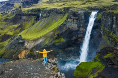 Sarı paltolu adam İzlanda 'daki Landmannalaugar Kanyonu' nda Haifoss Şelalesi 'ne hayranlıkla el kaldırdı. Havadan panoramik dron görüntüsü.