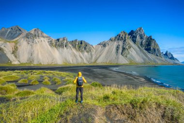 Sırt çantalı bir adam, Stoksnes Burnu 'nda, güneydoğu İzlanda sahilinde Vestrahorn' lu siyah kum tepeciklerinde yürüyor. Renkli yaz sabahı İzlanda, Avrupa.