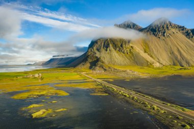 Uçan İHA 'nın görüntüsü. Arka planda Vestrahorn 'la Stoksnes' in büyüleyici manzarası. Panoramik İzlanda görüşü, siyah kum tepelerinin gelgitle sarı otlarla kaplı olması..