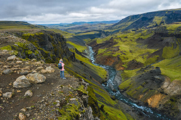 Aerial above view of woman with backpack enjoying icelandic highland and river fossa close to Haifoss waterfall in Iceland.