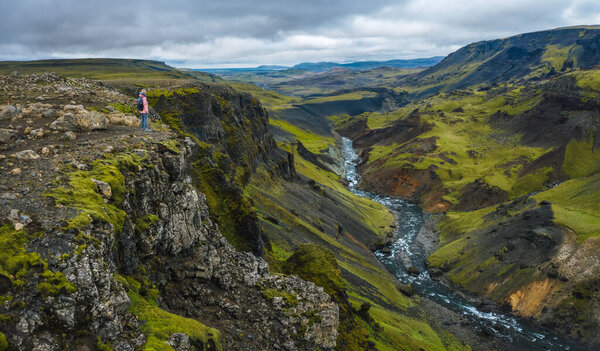 Aerial above view of woman with backpack enjoying icelandic highland and river fossa close to Haifoss waterfall in Iceland.
