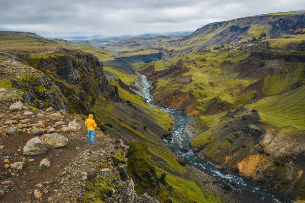 Aerial view of man enjoying Iceland landscape of highland valley and river Fossa with blue water stream and green hills and moss covered cliffs.