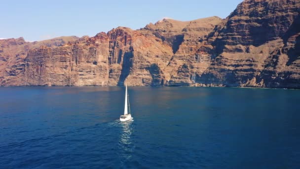 巨大的高山和一艘孤独的白色游艇在深蓝色蔚蓝的海水中漂流 晴朗的下午 空中俯瞰一艘小船 Tenerife加那利岛西班牙自然景观 — 图库视频影像
