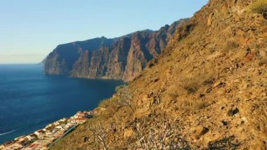 Sunset light illuminate steep Los Gigantes cliifs rocky barren volcanic mountains with dark blue deep ocean water. Sea, crags silhouette. Nature seascape. Paradise island Tenerife. Nobody.