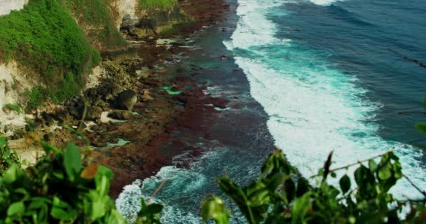 绿色的热带悬崖被蓝色的印度洋海水冲刷 形成白色的发泡波 印度尼西亚巴厘岛的Uluwatu岩滩 慢动作特写静态视图 — 图库视频影像