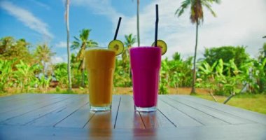 Two glasses of smoothies pudding with mango and dragon fruit banana on wooden table with nature background. Healthy vegetarian breakfast. Everyday life in travel.