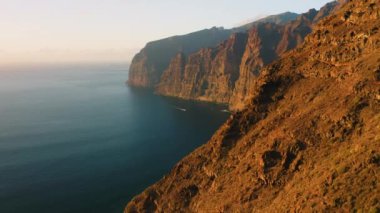 Spectacular ocean view with warm sunset light at Los Gagantes cliffs enormous crags. Flight along high volcanic rocky mountains Tenerife Canary Islands Spain Europe. Aerial footage. Nobody.