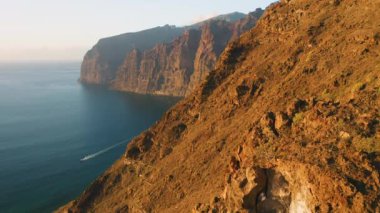 Warm sunset light at Los Gagantes cliffs with deep calm ocean. Flight along high rock crag mountains Tenerife Canary Islands Spain Europe. Aerial footage. Nobody.