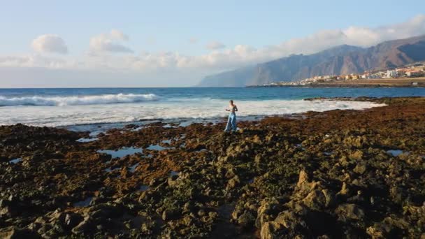 Girl Traveler Explores Walking Rocky Volcanic Beach Wide Foaming Waves — Stock Video