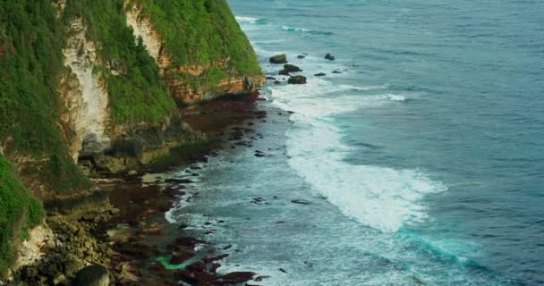 石灰岩の切り立った崖と紺碧のインド洋の波とバリ島の活気に満ちた熱帯海岸 ウルワツ岩礁のビーチ インドネシア スローモーションビュー 手持ちの映像 — ストック動画
