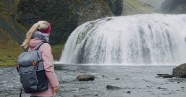 İzlanda, sırt çantalı kadın Kirkjubaejarklaustur yakınlarında Stjornarfoss şelalesinin keyfini çıkarıyor..