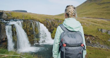 Kuzey İzlanda 'da Kirkjufellsfoss' un keyfini çıkaran kadın turistin arka görüntüsü.