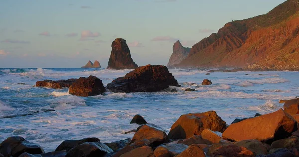 stock image Stony beach at evening. The waves crash on rocky shore, pebbles, volcanic basalt in Tenerife Island. Sea water splashes form white foam. Never-ending beauty of nature.