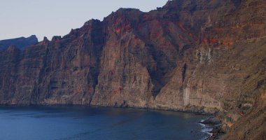 Los Gigantes uçurumları. Tenerife 'de gün batımı, Kanarya Adaları, İspanya. Kanarya Adaları 'ndaki volkanik kayalık sahil beldesi. Hiç kimse. Dağların manzarası yavaş yavaş açılır, çerçeve yatay olarak görünür. Tutulan görüntüleri sakla.
