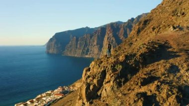 Hiker man standing on mountain top and enjoying ocean view at sunset. Boy looking at deep sea with huge rocky mountains Los Gigantes Tenerife. Adventure freedom exploration of Planet Earth. Canary