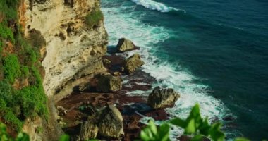 Relax ocean view with turquoise wide foam waves roll on rocky cliffs beach blue crystal clear water. Peaceful zen green nature background. Greenery, tropical plants in the foreground. Nobody. Calmness