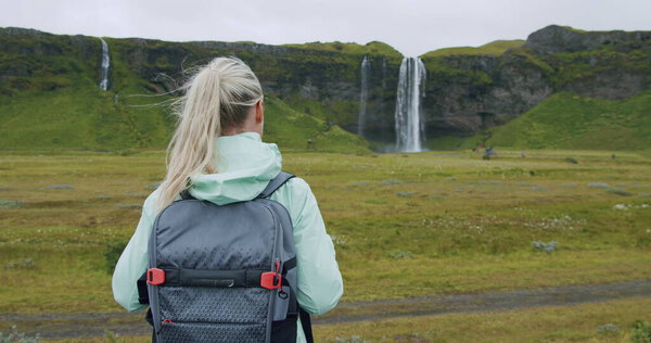 Woman with backpack looking at Seljalandsfoss waterfall Iceland.