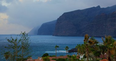 Canary Islands, Tenerife. Mountain resort town with many hotels, palm trees. Los Gigantes Cliffs. Sunny day. In the background Atlantic Ocean.