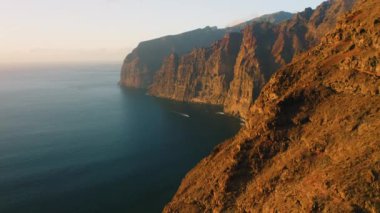 Warm sunset light at Los Gagantes cliffs with deep calm ocean. Flight along high rock crag mountains Tenerife Canary Islands Spain Europe. Aerial footage. Nobody.