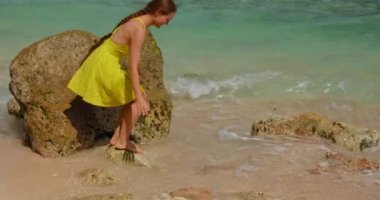 Woman enjoys on epic white sandy beach. Slow motion of ocean waves. Life on vacation on a tropical Bali island. Concept summer tourism holidays. Lonely girl washing her face with sea water.