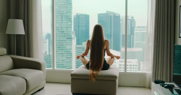 近代的な大都市の高層ビルを見下ろす窓から瞑想をリラックス成功した女性の背面ビュー 女の子が椅子に座ってビジネスの成功を楽しむ将来のビジョンの夢を考える — ストック動画