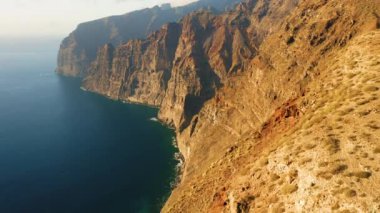 Dik uçurumlar volkanik dağlar İspanya 'nın Tenerife Kanarya Adaları' nın kıyı şeridini oluşturur. Los Gigantes derin mavi okyanus sularıyla sallanıyor. Gün batımında sinematik uçuş. İnanılmaz manzara..