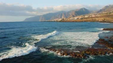 Aerial shot of empty rocky volcanic beach at the Atlantic Ocean in the soft morning light, flying low over the breaking waves. Tenerife Canary Islands Spain Europe.