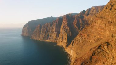 Sunset light at Los Gagantes cliffs and deep calm ocean. Volcanic mountains on Tenerife Canary Islands Spain Europe. Aerial footage.