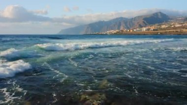 Ocean landscape with rocky coastline volcanic seaside of Punta Juanita Beach on Tenerife Canary Islands. Clouds on sky. Aerial flight over sea foamy waves crash on wild shore. Scenery. Amazing nature