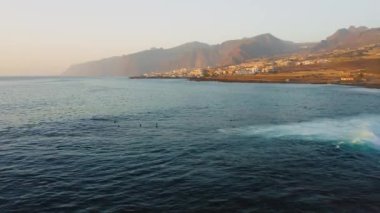 Azure ocean on Tenerife island at sunset. Giant mountain range covered with dense fog near to touristic place Los Gigantes.