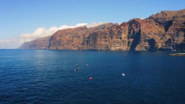 Ocean water with rocky coastline on Tenerife island. Giant mountain range Los Gigantes cliffs. Touristic water activity, kayaking.