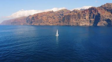 Sailing on yacht in sea against rocky volcanic cliffs Los Gigantes on Tenerife Island. Summer vacation in ocean. Boat journey. Canary Islands Spain Europe. Aerial view.