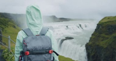 Güzel Gullfoss şelalesinin önünde sırt çantalı bir kadın gezgin. Meşhur turistik mekan ve İzlanda 'nın altın çember üzerindeki dönüm noktası.
