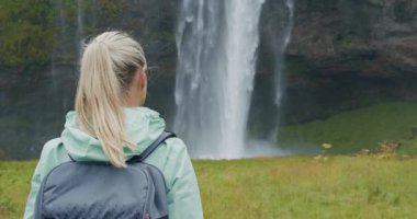 Güzel Seljalandfoss Şelalesi İzlanda 'ya giden sırt çantalı kadın gezginin yakın çekimi.