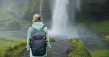 Sırt çantalı kadın Seljalandsfoss şelalesine doğru yürüyor.