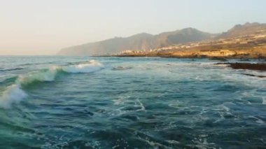 İspanya 'nın Tenerife Kanarya Adaları' ndaki kayalık volkanik kıyı şeridine deniz suyu çarpar. Geniş okyanus dalgaları köpük.