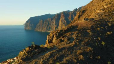 Adam okyanus manzaralı dik uçurumun kenarında duruyor. Yürüyüşçü dağın tepesine tırmanmayı deniz manzarasıyla kutluyor. Başarı zafer başarı konsepti.