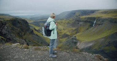 Sırt çantalı kadın İzlanda 'da Haifoss şelalesinin keyfini çıkarıyor.