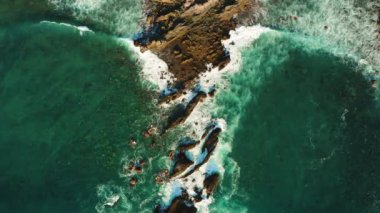 Zümrüt okyanus köpüğü ve deniz dalgaları kayalık volkanik plaja çarpar. Büyüleyici hava görüntüsü.