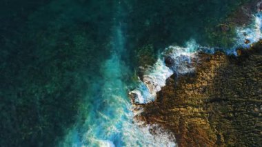 Okyanus dalgaları kayalık kıyı volkanik plajına çarpar. Yukarıdan aşağıya insansız hava aracı statik görüntüsü.
