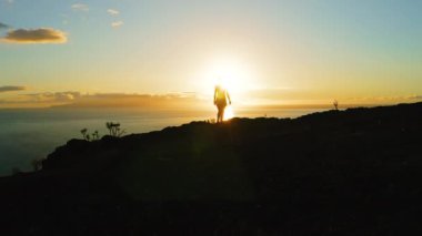 Kadın silueti bir dağa tırmanıyor ve gün batımında kollarını açıyor. Sonsuz okyanus renkli gökyüzüne karşı. Los Gigantes, Tenerife.