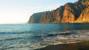 Tenerife Adası 'ndaki Playa de los Guios yüksek sarp kayalıkları olan Los Gigantes kumsalında okyanus dalgaları yuvarlanıyor. Turist eğlencesi. Siyah kayalık volkanik kıyı şeridi.