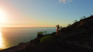 Kadın turist gün batımında dağ yamacına tırmanıyor. Hedefe ve başarıya ulaşmak. Tenerife 'de okyanus manzarası, Los Gigantes uçurumları.