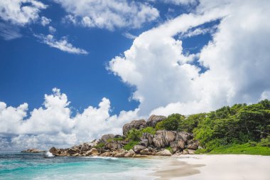 La Digue, Seyşeller 'deki Grand Anse tropikal plajı. Meşhur granit kaya oluşumları ve yukarıda beyaz bulutlar.
