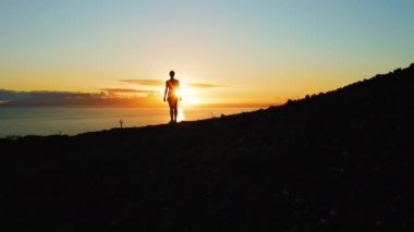 Dağ manzaralı, okyanusun üzerinde gün batımı. Yalnız kadın silueti. Renkli turuncu gökyüzünün havası. Los Gigantes Tenerife. Suyun üzerindeki güneş yolu.