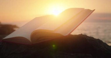 Gün batımında okyanus tarafından aydınlatılan açık bir kitap. Dünya Şiir Günü.