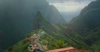 Güneş ışığı sislerin ve yağmurların arasından dağlık arazide Masca Vadisi 'ndeki küçük köy binalarıyla birlikte..